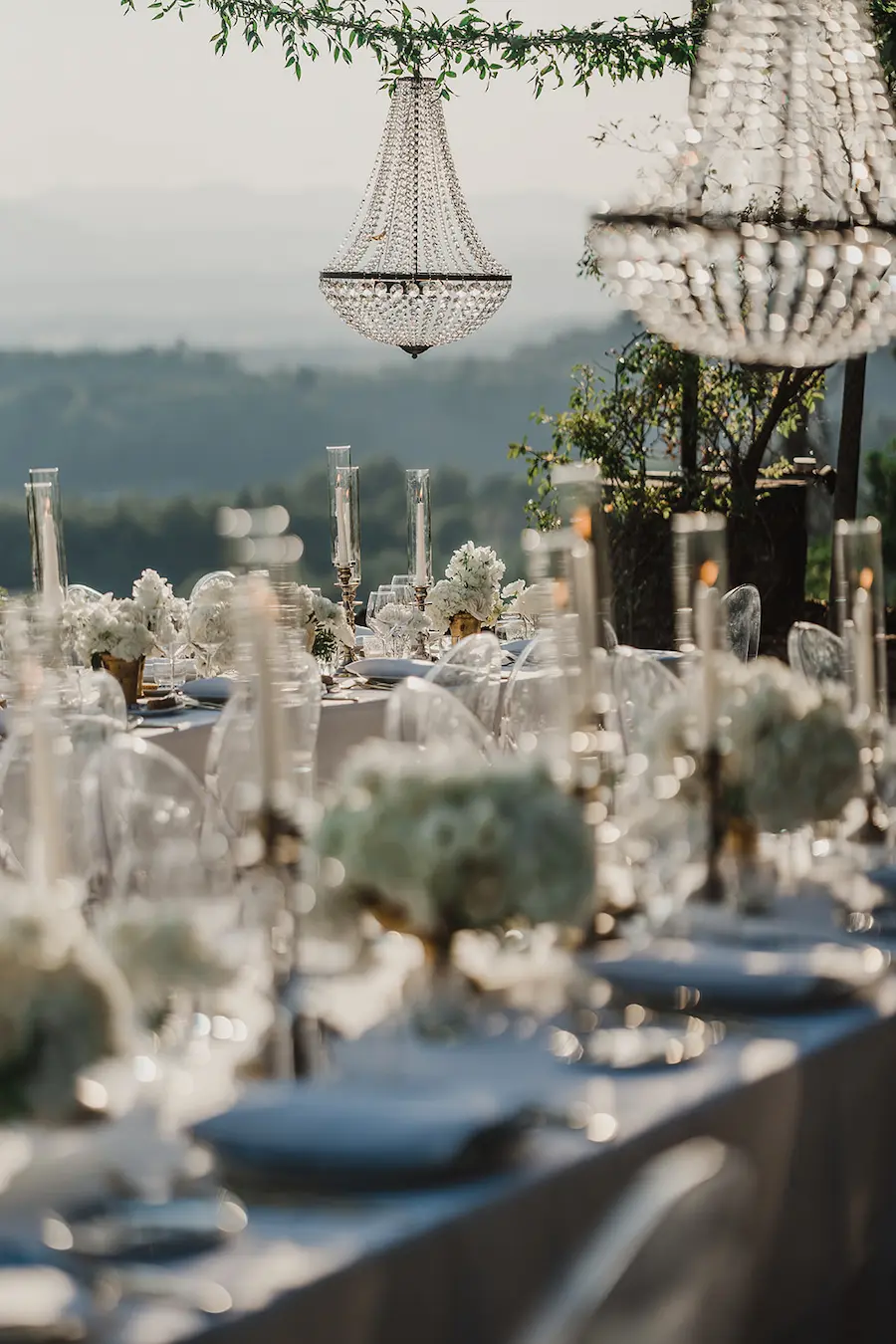 Luxuriöses Hochzeitskonzept mit Kerzenlicht & Panorama Hochzeitstafel mit Kronleuchtern, Kerzen und weißen Blumen im Freien – Inspiration für exklusive Wedding Planner