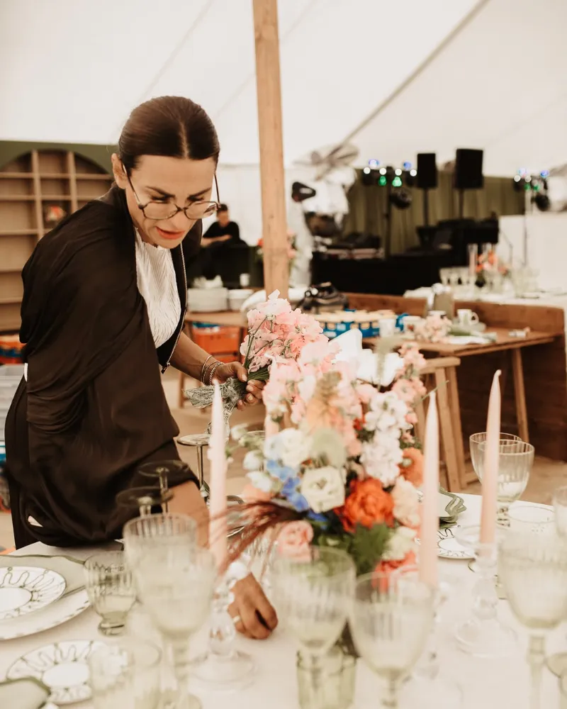 Kornelia Cimtsaris von Verleih & Dekoration richtet Blumen auf einer festlich gedeckten Hochzeitstafel