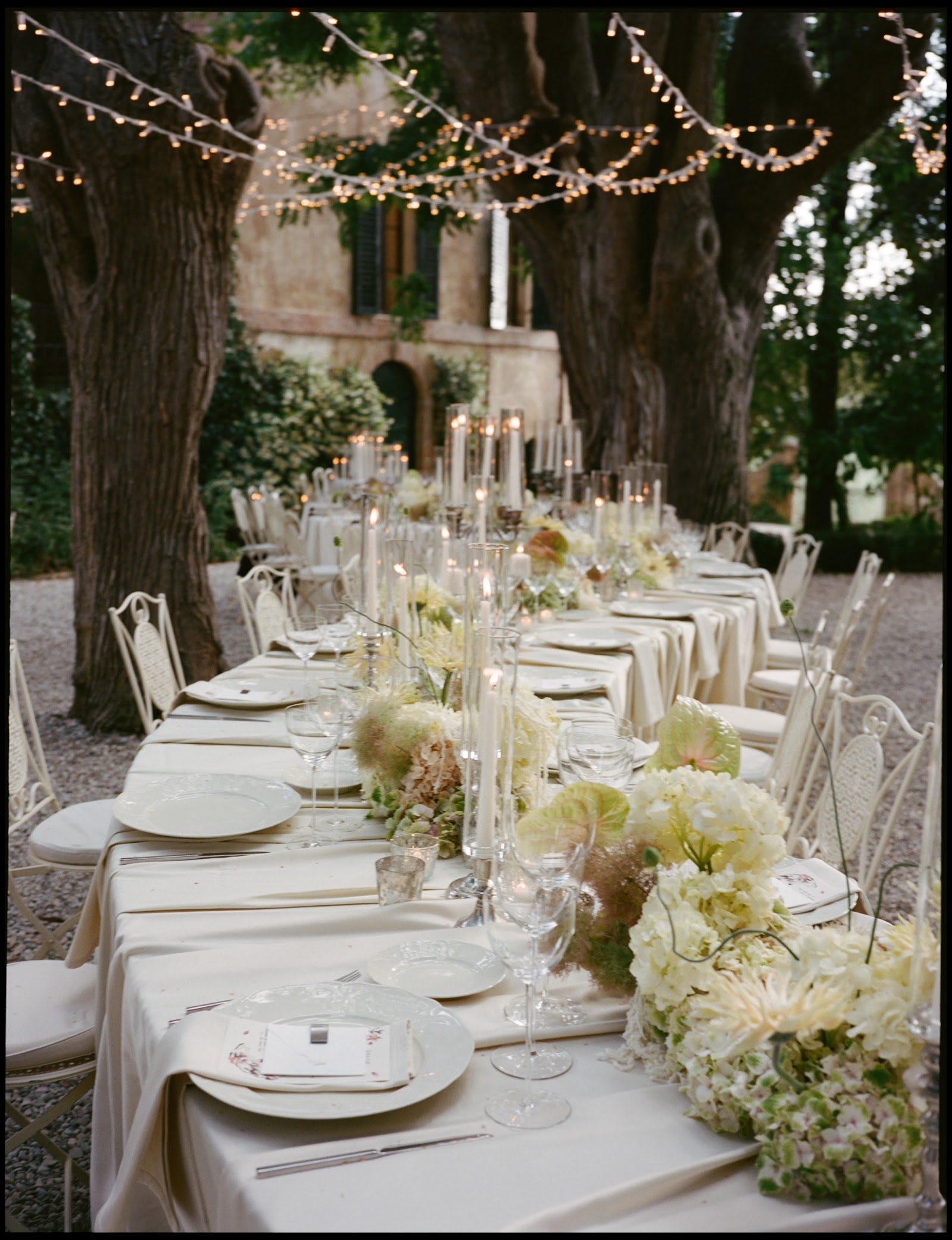 Lange Hochzeitstafel unter Lichterketten im Garten einer Villa
